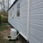 Zijaanzicht chalet met buitenunit airco op opstelblokken en leidinggoot langs gevel
