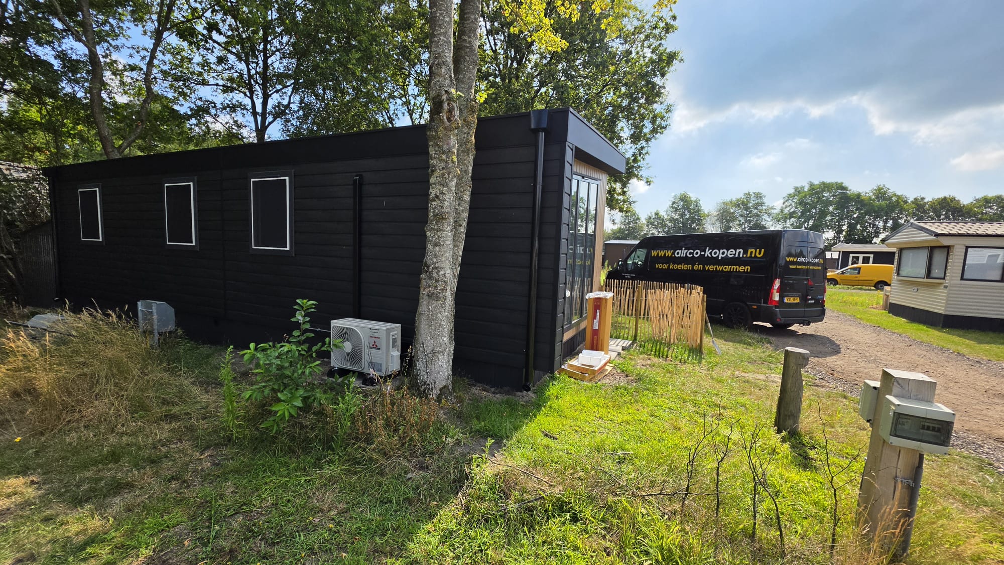 Zwart chalet op Camping De Reeënwissel met geplaatste Mitsubishi Heavy Industries airco en bus van Airco-Kopen.nu