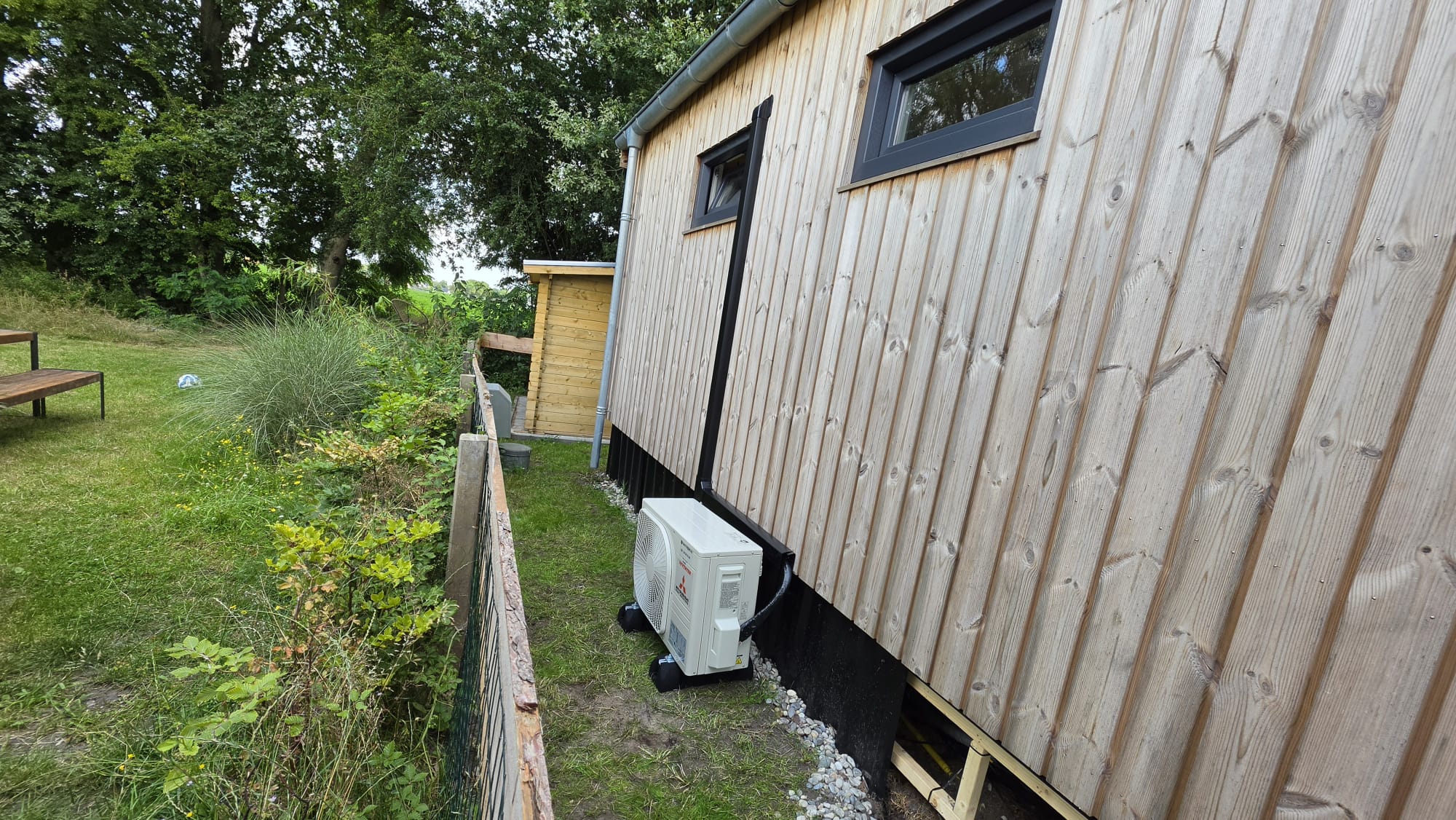 Mitsubishi Heavy Industries buitenunit op de begane grond naast Tiny House Bosplekkie op Camping De Reeënwissel in Hoogersmilde