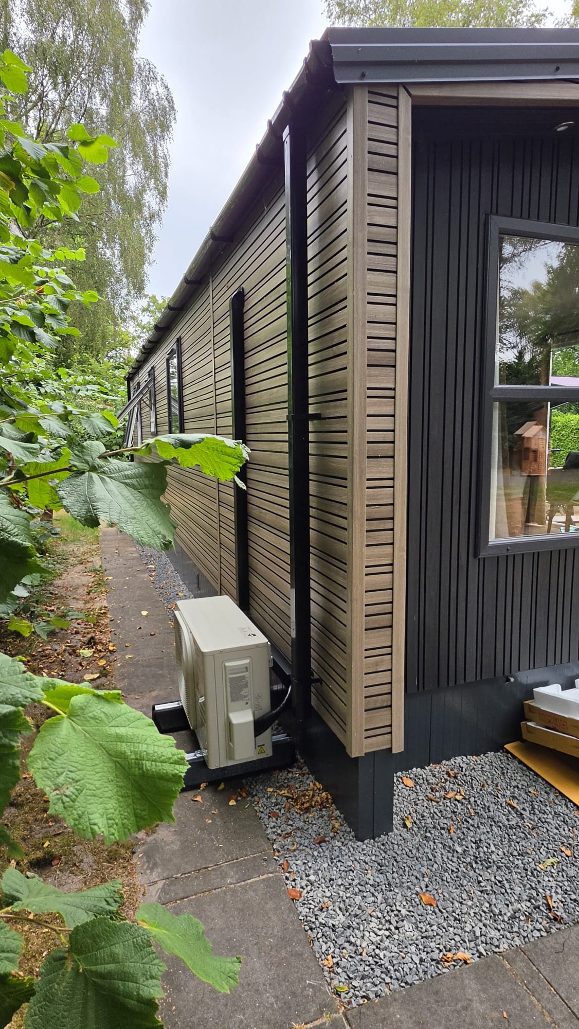Buitenunit van Mitsubishi Heavy Industries airco op de grond achter chalet op Camping De Klimberg