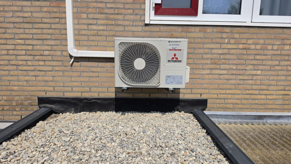 Mitsubishi Heavy Industries buitenunit aan gevel boven plat dak van uitbouw in Wezep